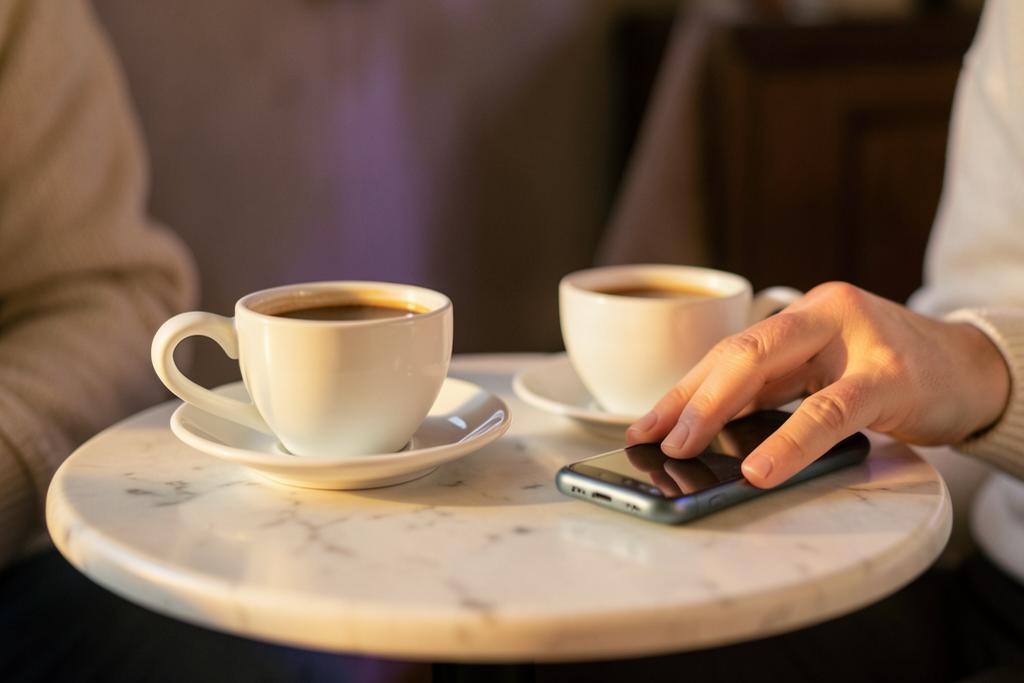 Two coffee cups on a marble cafe table with a hand resting next to a face-down phone